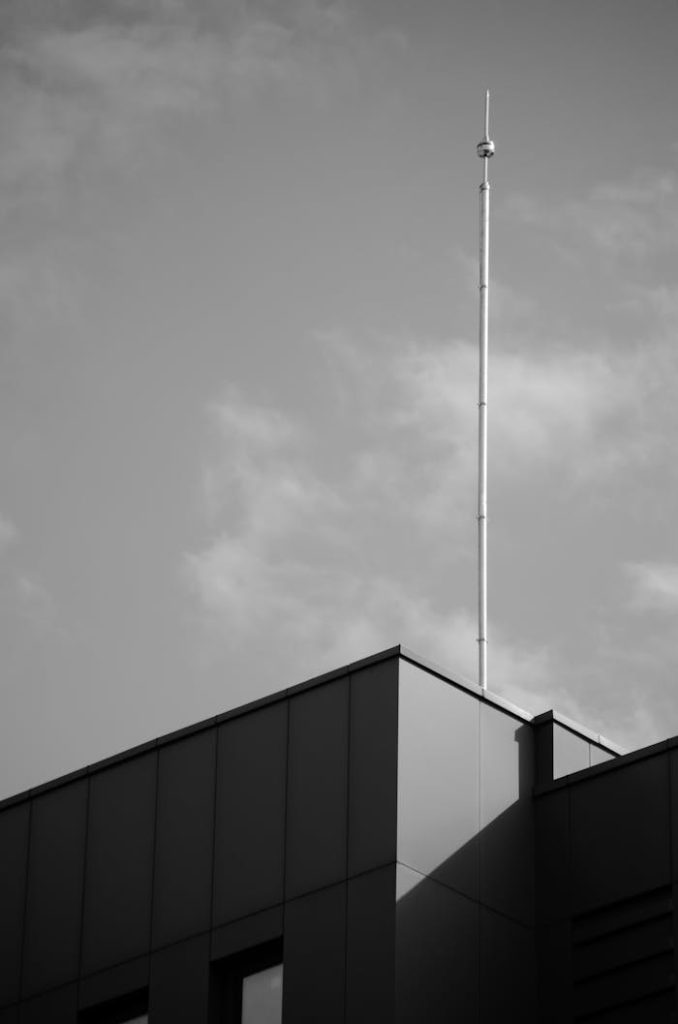 Black and white photo of a modern rooftop with a tall antenna reaching into a clear sky.