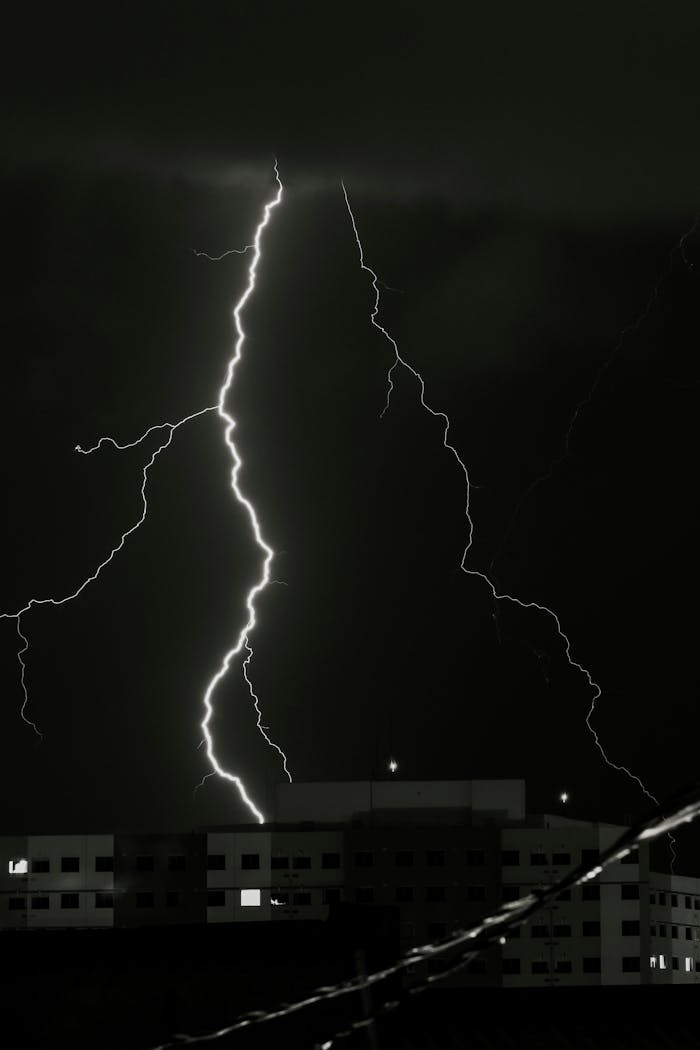 A striking lightning bolt illuminates the sky above buildings during a stormy night.
